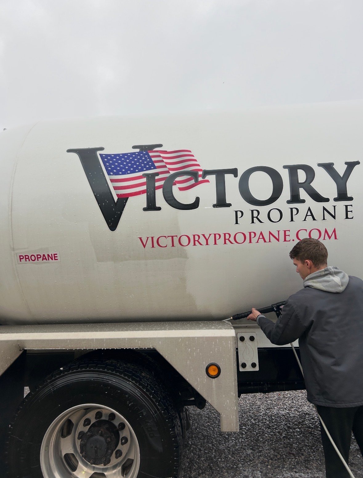 Worker standing beside white Victory Propane delivery truck with American flag logo and company website